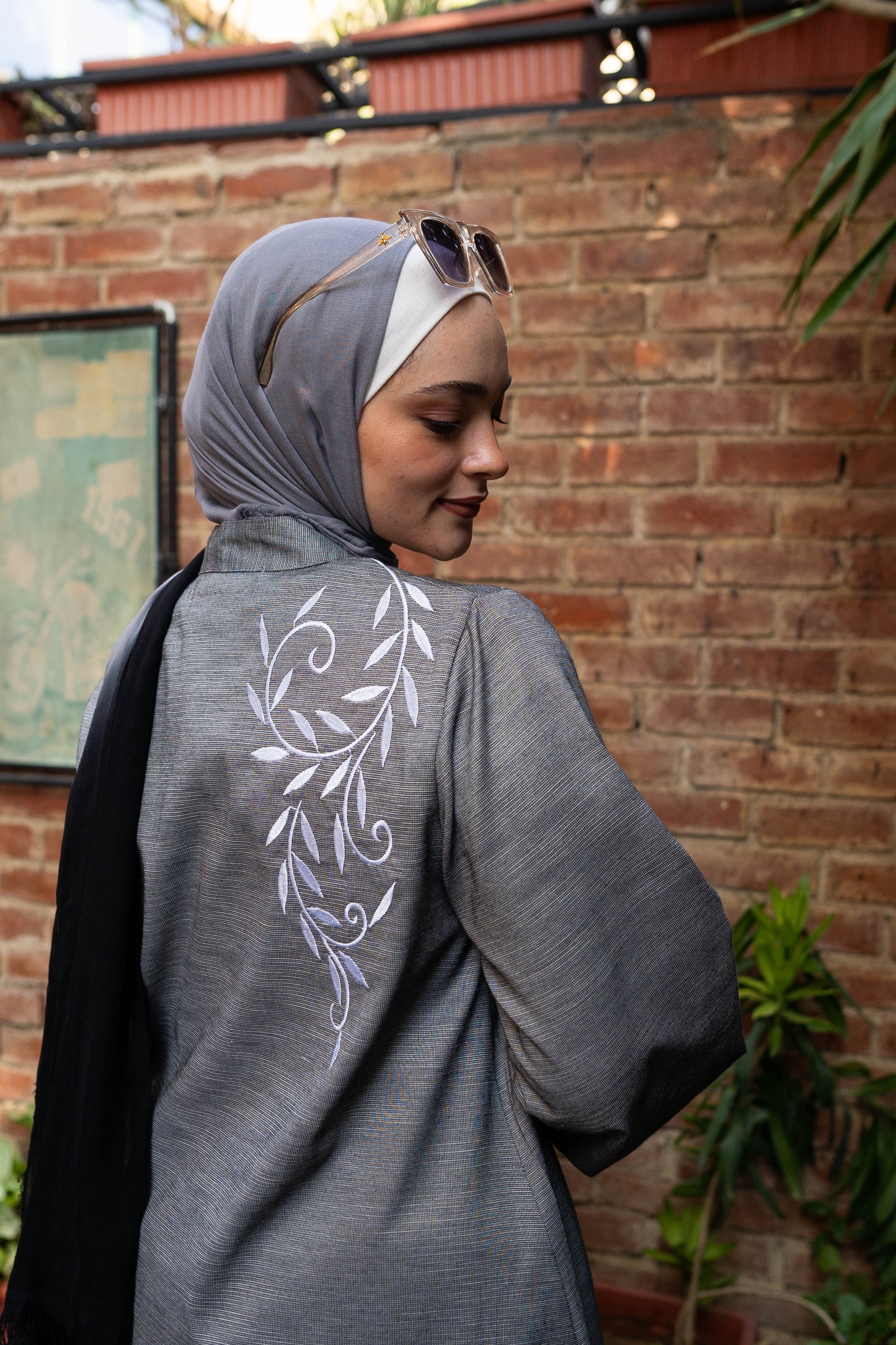 Back view of Long Shirt in Gray featuring the button-down design and long sleeves. قميص طويل باللون الرمادي مع تصميم الأزرار الأمامية وأكمام طويلة، منظر خلفي.