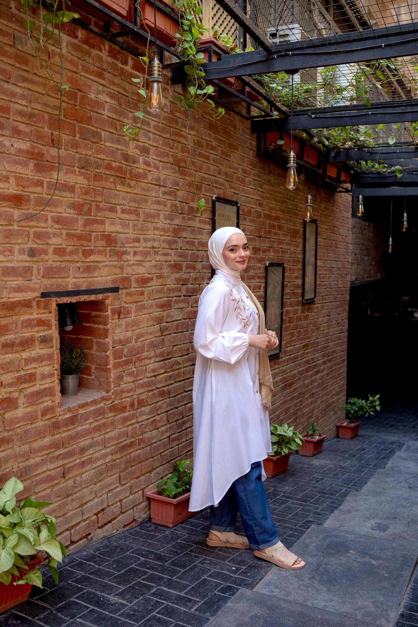 Side view of Long Shirt in White showcasing the relaxed fit and long sleeves. قميص طويل باللون الأبيض يظهر التصميم المريح والأكمام الطويلة، منظر جانبي.